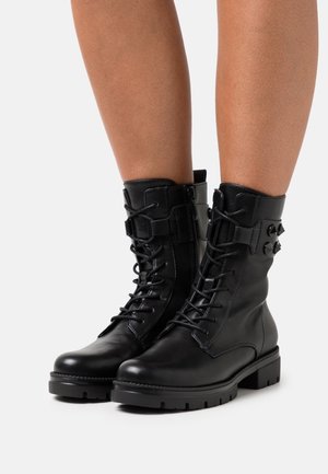 Black leather ankle boots with a lace-up front, side zippers, and chunky rubber soles. Features decorative straps and buckles.