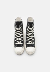 Black high-top sneakers made of canvas with white shoelaces, contrasting stitching, and a white rubber toe cap.