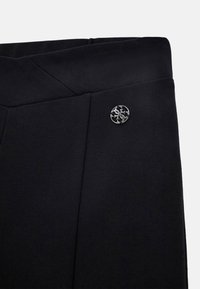 Pantaloni sportivi neri con una texture liscia, caratterizzati da un accento del logo argentato e un design della vita angolato unico.