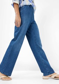Blue wide-legged denim pants with a high waist, featuring a smooth texture and side pockets. Worn with light-colored sandals.