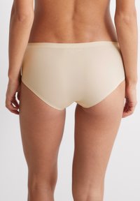 Naadloze nude hipster ondergoed gemaakt van gladde, rekbare stof, met een low-rise tailleband en een minimalistisch dekkingsontwerp.