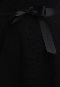 Tissu en dentelle noire avec des motifs floraux, noué avec un ruban de satin noir lisse.