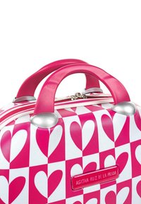 Maleta rígida con un patrón de corazones en rosa y blanco, con asas dobles en rosa y detalles en plata, que incluye una cremallera y una placa de nombre de la marca.