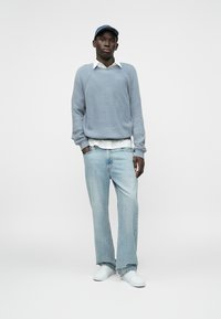 Gaiši zils ribota džemperis, balta apkakles krekla, gaiši zili džinsi un baltas sporta kurpes. Modelis valkā zilu cepuri. Vienkāršs un ikdienišķs dizains.