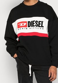 Svart och vit sweatshirt med röda detaljer, prydd med en djärv "DIESEL"-logotyp och texten "DENIM DIVISION", tillverkad av mjukt material.