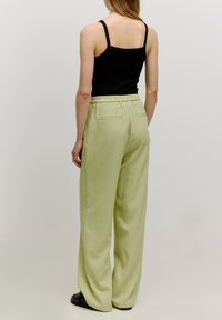 Pantalons larges vert clair avec une taille élastique, deux poches arrière et une texture lisse, associés à un débardeur noir.