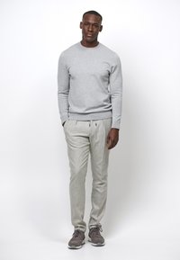 Felpa grigia, pantaloni grigi chiari con pence, fit slim e sneakers. Tessuto liscio, design minimalista e palette di colori neutri.