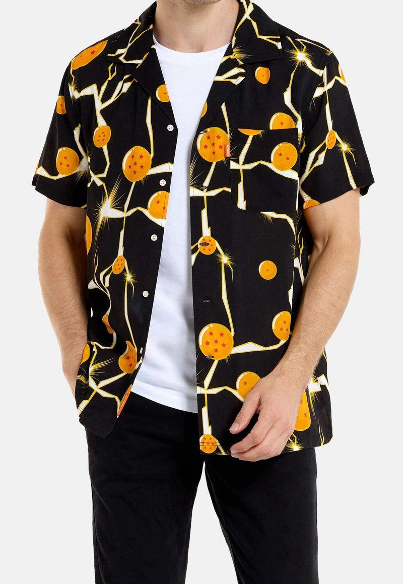 Homme portant une chemise noire à manches courtes boutonnée avec un motif de balle orange et d’éclair par-dessus un t-shirt blanc.