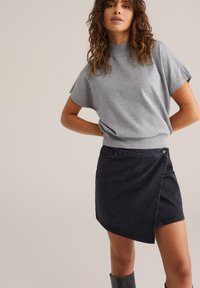 Maglione grigio a maniche corte con collo alto abbinato a una gonna avvolgente in denim scuro con orlo diagonale e bottone decorativo.