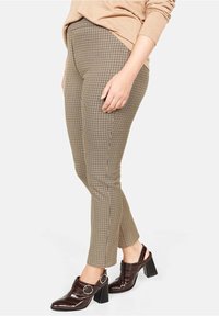 Pantaloni a scacchi marroni e beige con vestibilità slim, caratterizzati da un'alta vita e una trama delicata, abbinati a scarpe con tacco scure.