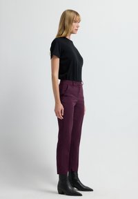Un haut noir à manches courtes associé à un pantalon bordeaux ajusté ; le pantalon comprend des poches latérales et une taille ajustée, complété par des bottines noires.