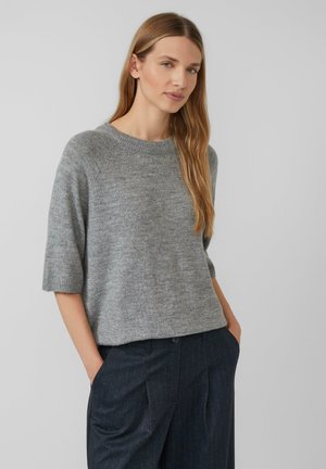 Pull en tricot gris clair avec un col ras du cou et des manches courtes. Texture douce, coupe décontractée, porté avec un pantalon à rayures noires.