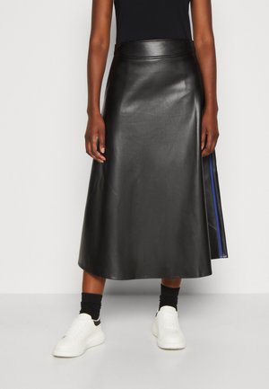 Osoba nosząca czarną midi spódnicę z ekoskóry z niebieskim paskiem, czarne skarpetki, białe trampki i czarny top bez rękawów.