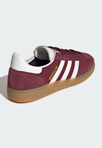 Burgundy velúr sportcipő fehér bőr díszítéssel, három fehér csíkkal és barna gumi talppal; oldalán arany "SPEZIAL" felirattal.