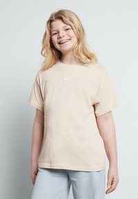 Bež majica iz bombaža s kratkimi rokavi in okroglim izrezom. Ima majhen bel Nike logotip na prsih. Preprost in sproščen dizajn.