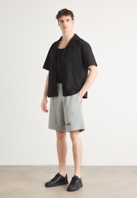 Camisa negra de manga corta con un patrón texturizado, combinada con pantalones cortos gris claro hasta la rodilla y zapatillas negras. Estilo casual, con un ajuste relajado.