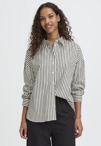 Raiškus mėtinio žalia ir baltos spalvos dryžuotas marškinis, su mygtukais, ilgomis rankovėmis ir laisvu siluetu. Minkšta medžiaga su švelniu tekstūra.