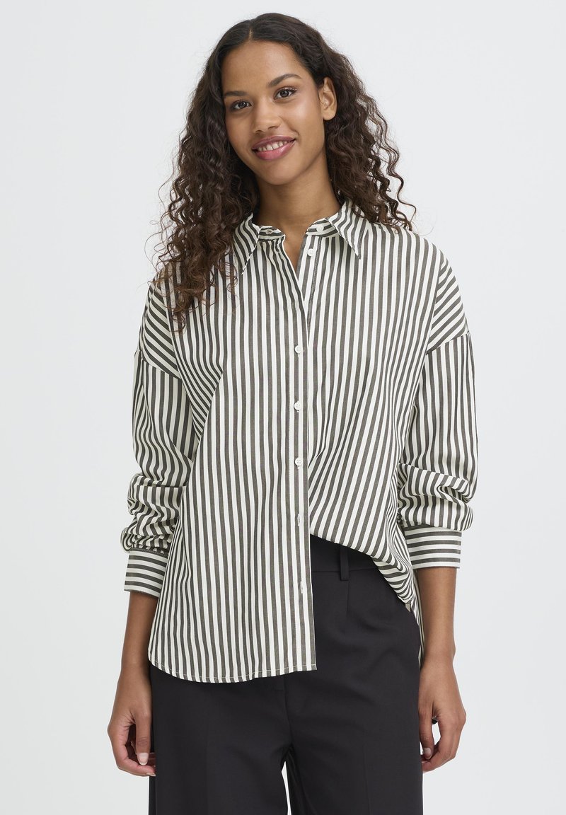 Raiškus mėtinio žalia ir baltos spalvos dryžuotas marškinis, su mygtukais, ilgomis rankovėmis ir laisvu siluetu. Minkšta medžiaga su švelniu tekstūra.