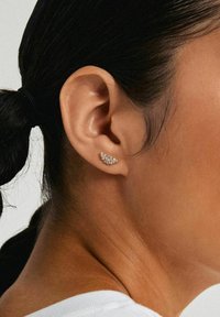 Goldfarbener Ohrstecker mit einem Cluster aus kleinen klaren Kristallen, der ein gewundenes Design aufweist, das sich um das äußere Ohr legt. Glatte metallische Oberfläche.