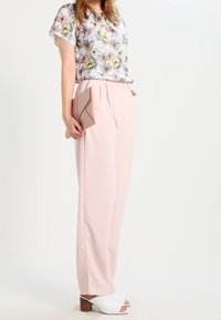 Lichte bloemenblouse met korte mouwen, gecombineerd met lichtroze hoge taillebroek. Geaccessoireerd met een roze clutch en witte hakken.