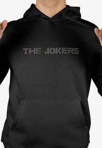Sudadera negra con capucha que presenta "THE JOKERS" en texto plateado con tachuelas. Tiene un bolsillo delantero y capucha con cordón. Tela suave con un diseño sencillo.