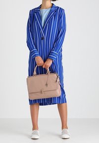 Blå och vit randig lång jacka, håller en ljusrosa läderhandväska med klaff och detaljer i metall, samt vit perforerad skor.