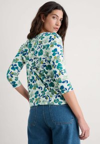Haut à manches trois-quarts fleuri en vert clair, présentant des motifs botaniques bleus et verts. Tissu doux et texturé avec une coupe décontractée.