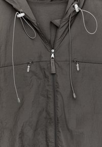 Ciemnoszara kurtka z kapturem, z centralnym zamkiem błyskawicznym, dwoma małymi kieszeniami na zamek oraz regulowanymi sznurkami z plastikowymi stoperami przy kapturze.