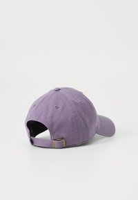 Lilla bomulds-baseballcap med buet skygge, justerbar rem bagpå og knapdetalje på toppen; glat tekstur.