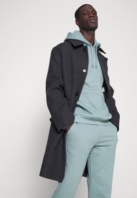 Donkergrijze wollen jas met een relaxte pasvorm, met een enkele knoopsluiting, gelaagd over een lichtblauwe hoodie en bijpassende joggingbroek.