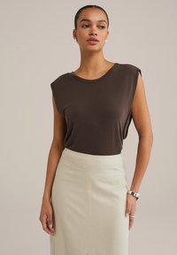 Brun ärmlös topp i ett mjukt material med rund halsringning, som kombineras med en ljusbeige kjol. Enkel design, minimal detaljer, slät textur.