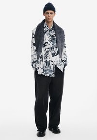 Black oversized pants paired with a white and black patterned shirt and a grey scarf, complemented by a dark beanie and black shoes.