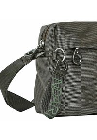 Primo piano di una borsa in tessuto nero e grigio con una texture, dotata di zip in metallo e un'etichetta in tessuto verde con la scritta "INDARY" attaccata.