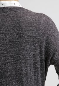 Vue de dos d'une personne portant un pull duveteux gris foncé superposé sur une chemise blanche avec des motifs d'étoiles noires sur le col.