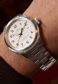 Timex vízálló óra ezüst színű rozsdamentes acél tokkal, fehér számlappal, fekete arab számokkal, dátumkijelzővel és fém szíjjal.