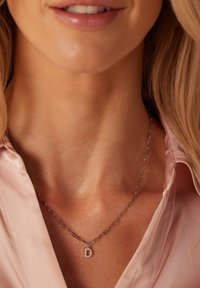 Zilveren ketting driehoekjes met verlengde schakels en een kleine hanger met de letter "D." Draagt over een lichtroze stof.