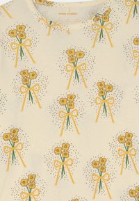Helle Baumwollbluse mit einem wiederholten Muster aus gelben Blumen, die mit grünen Schleifen gebunden sind, akzentuiert mit schwarzen Sprenkeln.