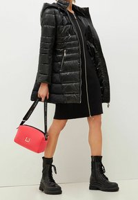 Czarna pikowana kurtka z kapturem, czarna dopasowana sukienka, czarne botki wojskowe oraz różowa torebka z logo i regulowanym paskiem.