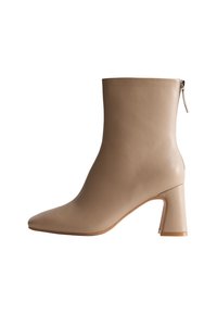 Beige leren enkellaars met een spitse neus, ritssluiting en een chunky hak, met een gladde textuur en minimalistisch ontwerp.