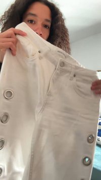 White denim pants with large silver grommets down the sides, featuring a fitted design and classic five-pocket styling.
