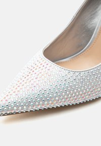 Ασημένιο μπαλαρίνα με αιχμηρή μύτη, καλυμμένη με μικρά ιριδίζοντα στρας και λείο εσωτερικό επένδυμα.