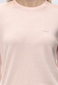 Pull tricoté rose clair avec un petit logo brodé sur le haut gauche de la poitrine et un col rond.