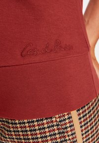 Bordeauxrotes Baumwolloberteil mit gesticktem "Casual Strides"-Logo. Verfügt über ein tailliertes Design und eine glatte Textur, kombiniert mit Hahnentritt-Musterhosen.