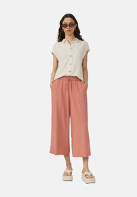 Crème kleurig shirt met korte mouwen en knopen, gecombineerd met losse, roze wijde broeken met een elastische tailleband. Gedirigeerd met witte plateau-sandalen.