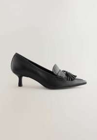 Scarpa nera in pelle con tacco medio e punta appuntita, dotata di un accento intrecciato e un pon-pon sulla parte anteriore. Texture liscia, design elegante.