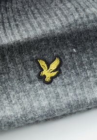 Gray knitted fabric with ribbed texture and a yellow embroidered flying eagle patch bordered in black.
