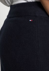 Marineblauwe gebreide sweatpants met een geribde tailleband, voorzien van een klein rood, wit en blauw logo accent nabij de heup. Zachte textuur.