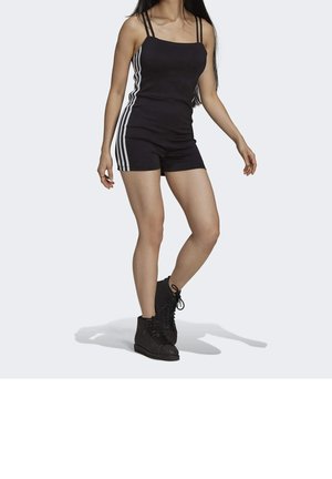 Černý sportovní overal s tenkými ramínky, se bílými bočními pruhy a přiléhavým střihem. Kombinován s černými šněrovacími botami, zobrazen na neutrálním pozadí.