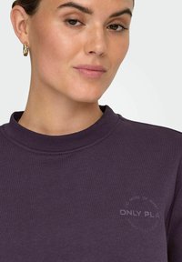 Mørkelilla sweatshirt med rund halsudskæring og minimalistische tekstdetaljer på brystet. Glat tekstur og afslappet pasform.