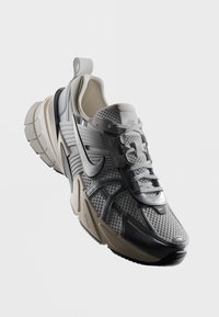 Chaussure de course Nike grise et beige avec tige en mesh, semelle épaisse segmentée et logo Nike noir bien visible sur le côté.